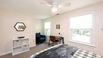 A bedroom with a bed, a desk, a chair, a ceiling fan, and a window.