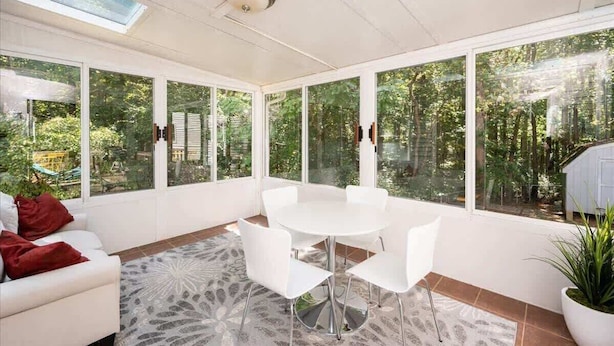 A sunroom with a round table and chairs, large windows, and a ceiling fan. - Quiet Retreat - Piano, Firepit, Peloton (Pittsboro)