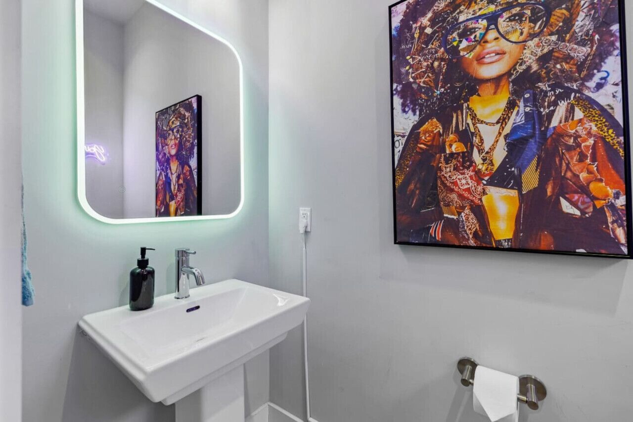 Une salle de bain avec un lavabo blanc, un miroir et une œuvre d ’art encadrée accrochée au mur.