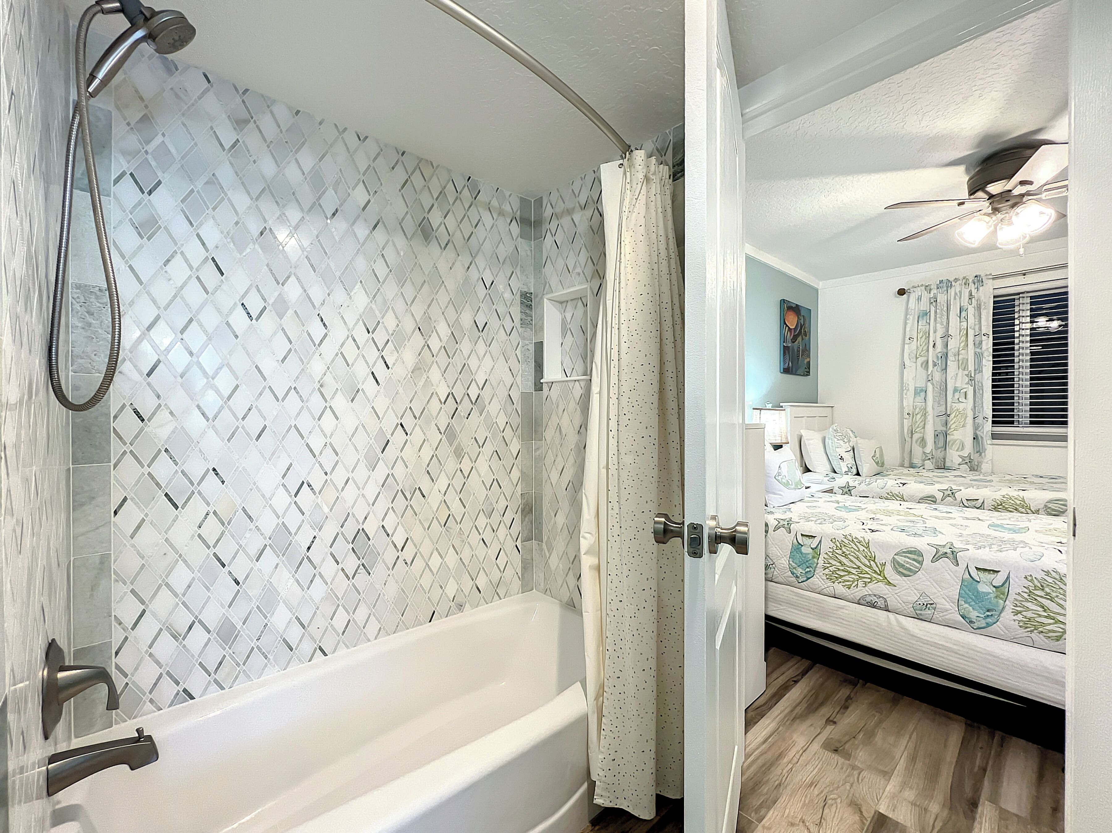 A bathroom with a bathtub, shower, and a bed with a nautical-themed bedspread.