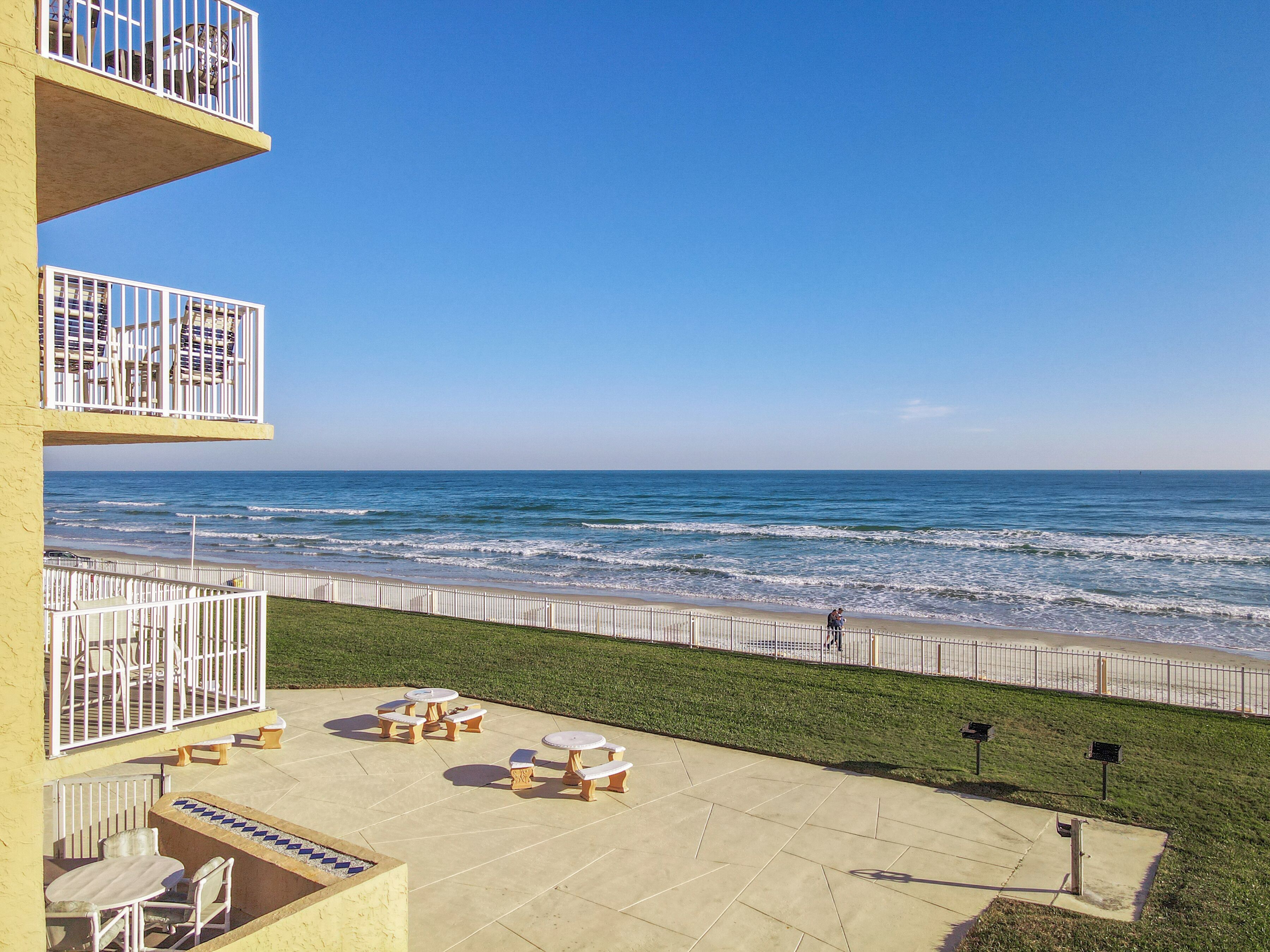 Un patio frente a la playa con mobiliario exterior y vistas al océano.