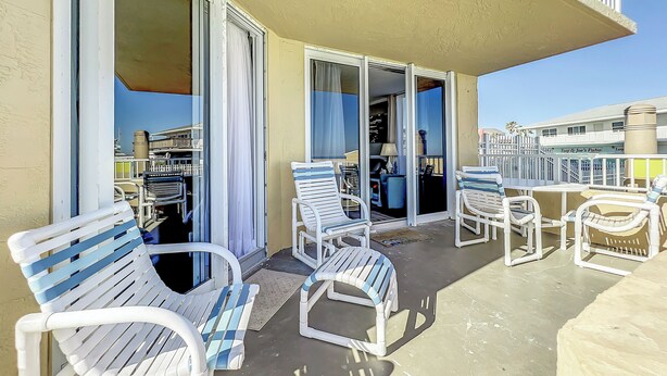 A balcony with white plastic chairs and a table, a sliding glass door, and a view of the sea. - Oceania Beach Club 106 (New Smyrna Beach)