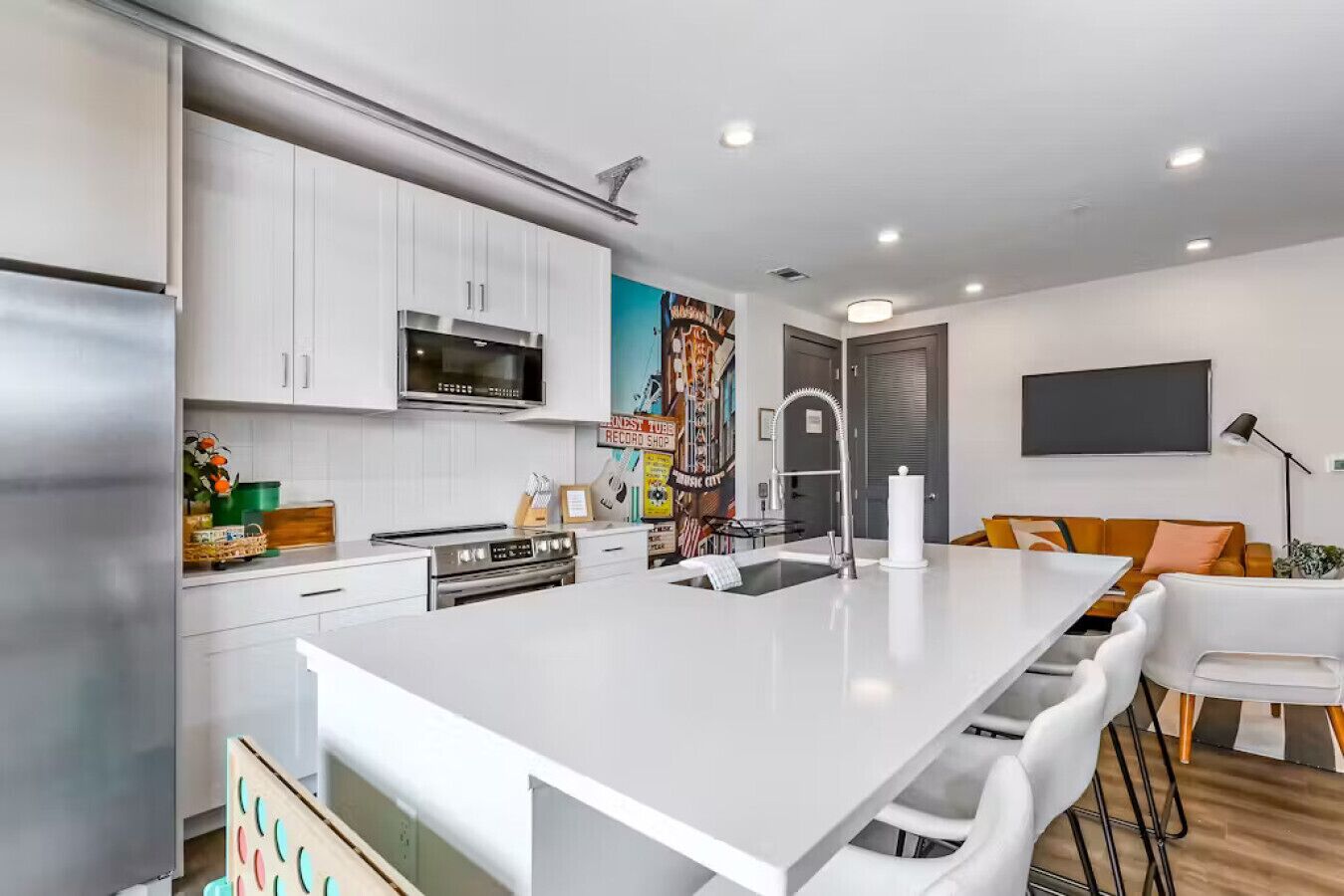 Una cocina moderna con armarios blancos, una isla central, electrodomésticos de acero inoxidable y un mural colorido.