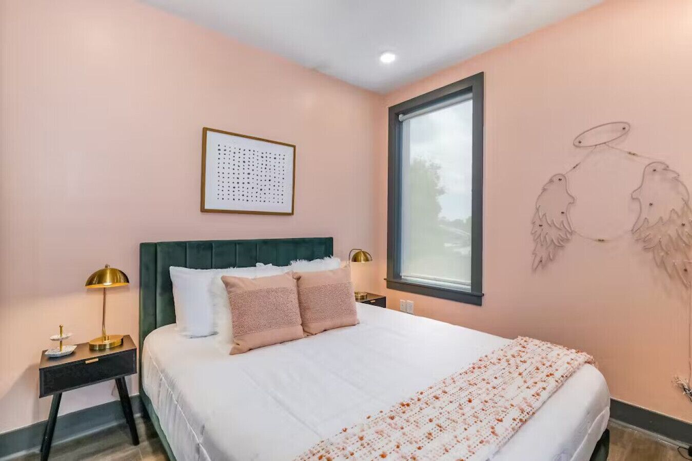 A bedroom with a bed, two bedside tables, a window, and a wall art piece.