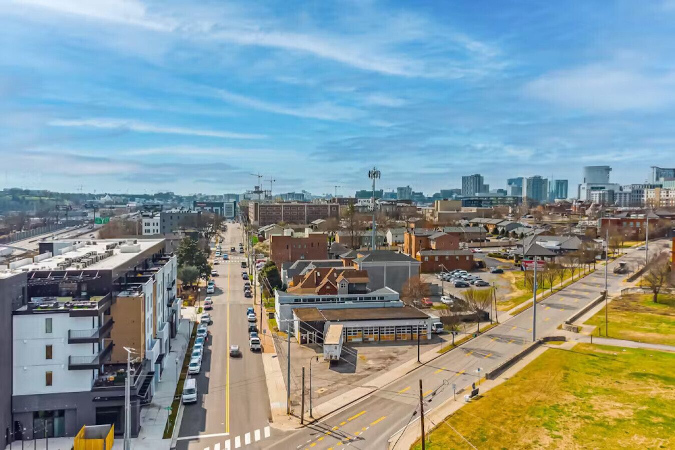 A cityscape with a mix of modern and older buildings, a wide street, and a clear sky.