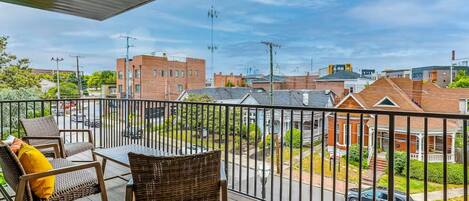 A balcony with wicker furniture and a view of a residential area with brick houses and a street.