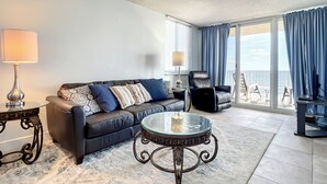 A modern living room with a leather sofa, glass coffee table, and a view of the balcony. - Oceania Beach Club 606 (New Smyrna Beach)