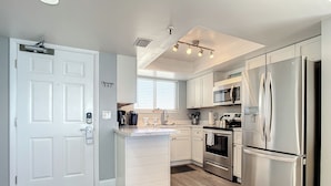A modern kitchen with white cabinetry, stainless steel appliances, and a wooden floor. - Oceania Beach Club 706 (New Smyrna Beach)