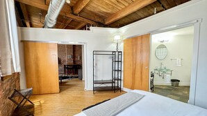 Camera da letto con un letto grande, soffitto in legno, parete in mattoni e bagno con lavandino in vetro.