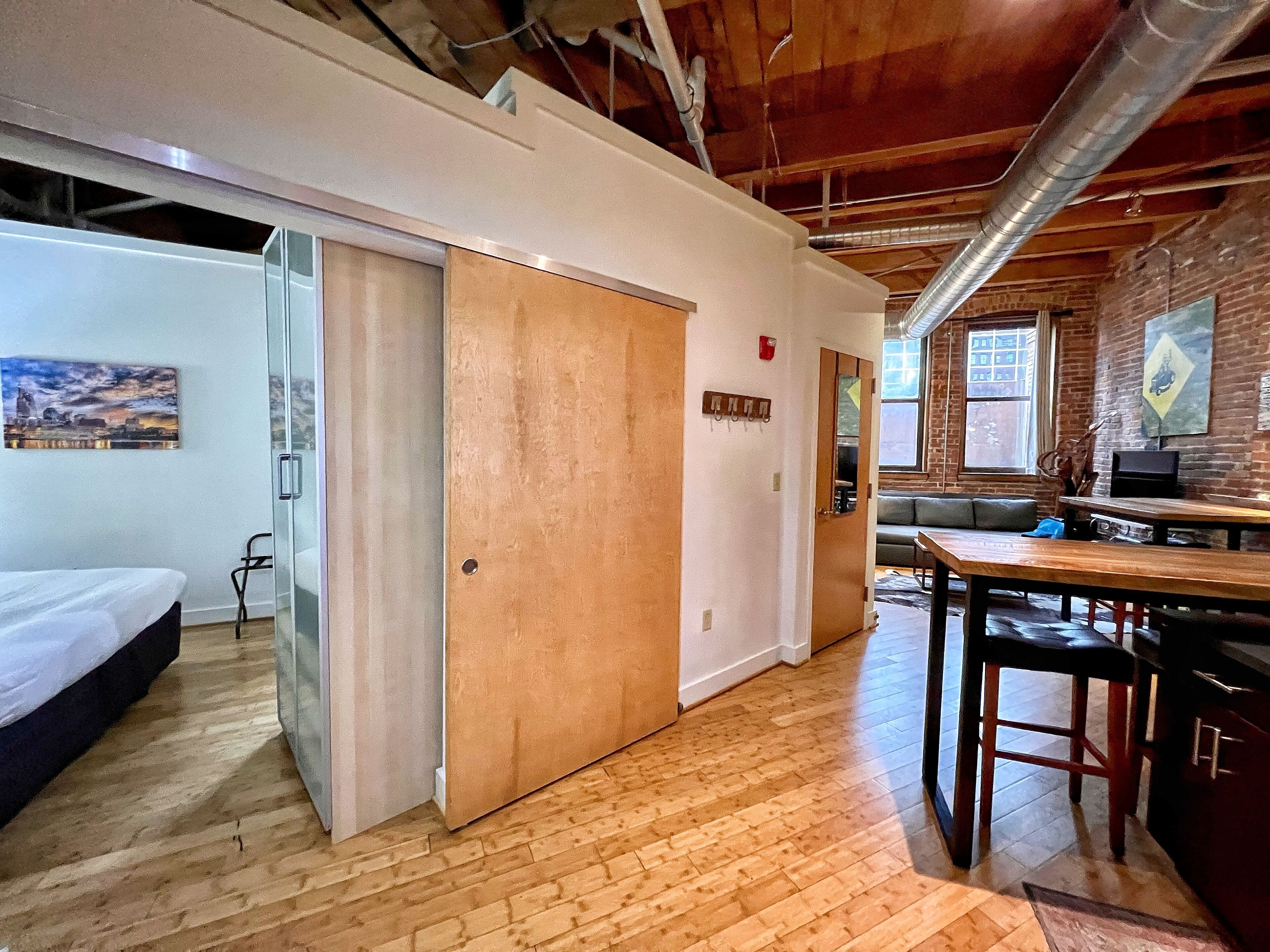 A room with a bed, a wooden door, a small table, and a chair.