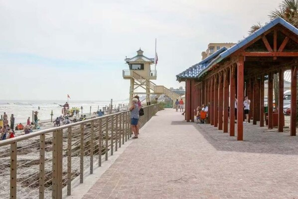 A beach promenade with a lifeguard tower, wooden walkway, and beachgoers. - Oceania Beach Club 303 (New Smyrna Beach)