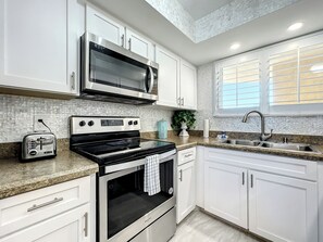 A modern kitchen with white cabinetry, a stainless steel microwave, a black oven, and a granite countertop. - Oceania Beach Club 409 (New Smyrna Beach)