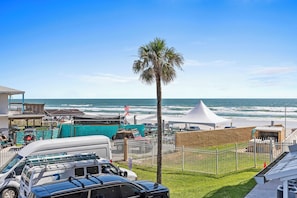 Une vue sur la plage avec une tente blanche, des véhicules garés et un palmier.