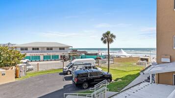 Um estacionamento com um SUV preto, uma van branca e um carro branco. Há um edifício com uma placa que diz “Tony & Joe's Patio”. Uma palmeira é visível e o oceano ao fundo.