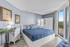 Une chambre avec un grand lit, une table de chevet, une commode, une plante en pot et un balcon avec vue.