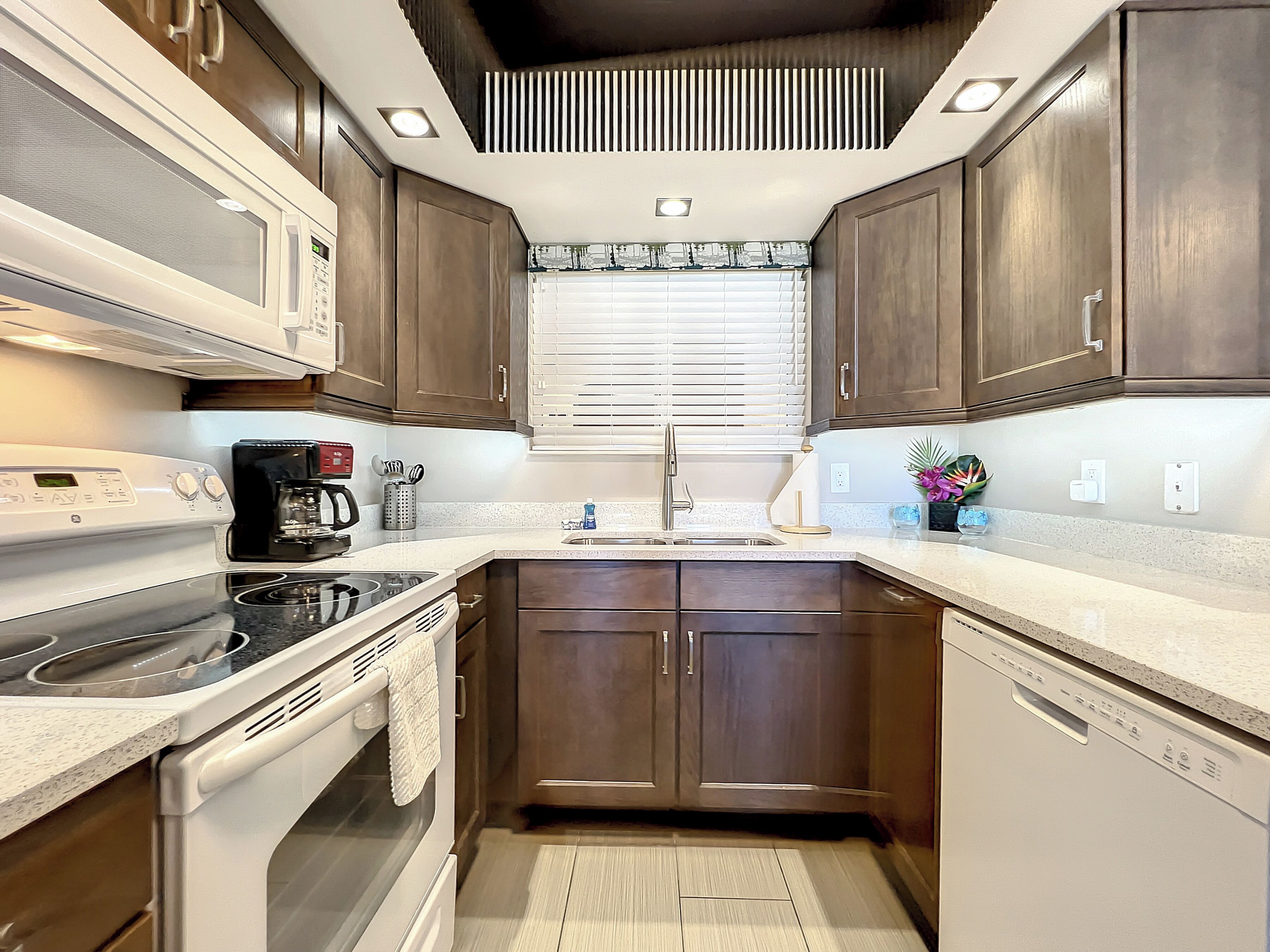 A compact kitchen with dark wooden cabinets, a white countertop, a built-in microwave, a stove, and a dishwasher.