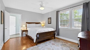 A bedroom with a wooden bed, two bedside lamps, a ceiling fan, and a window with blinds. - Neighborhood Retreat - Large Yard Family Fire Pit (Nashville)