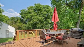 A wooden deck with a table and chairs, a red umbrella, and a grill. - Neighborhood Retreat - Large Yard Family Fire Pit (Nashville)