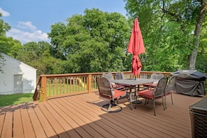Une terrasse en bois avec une table et des chaises, un parasol rouge et un barbecue.