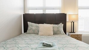 Un letto rifatto con biancheria a motivi, un asciugamano piegato sul letto e una lampada da comodino.