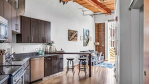 A modern kitchen with dark cabinets, a stainless steel sink, and a wooden ceiling. There is a dining area with a table and chairs. - June (Nashville)