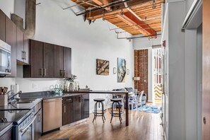 A modern kitchen with dark wooden cabinets, a stainless steel sink, and a wooden ceiling. There are two bar stools and a dining table. - June (Nashville)
