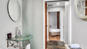 A modern bathroom with a glass sink, a mirror, and a shower area visible through an open door. - June (Nashville)