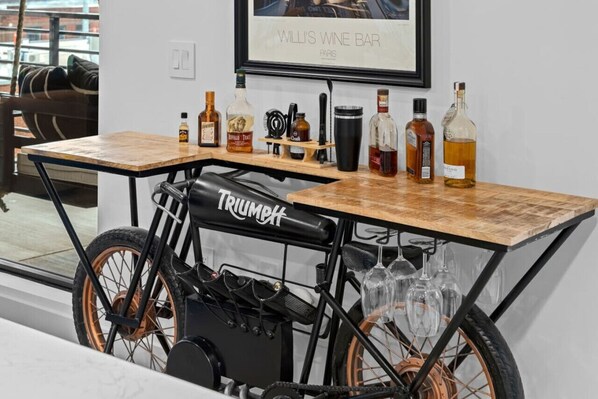 A bicycle cart with a Triumph logo, a wine bottle, and glasses on a table in a room with a framed picture on the wall. - Skyline Glory - With Pool in Downtown Nashville (Nashville)