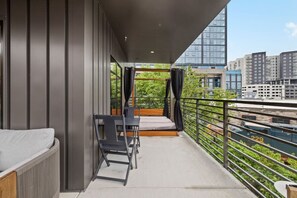 A balcony with a sofa, chairs, and a table. It overlooks a cityscape with buildings and greenery. - Skyline Glory - With Pool in Downtown Nashville (Nashville)