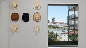 A room with a wall-mounted display of cowboy hats and a window overlooking a cityscape. - Skyline Glory - With Pool in Downtown Nashville (Nashville)