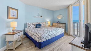 A bedroom with a bed, bedside tables, a TV, and a view of the sea. - Oceania Beach Club 503 (New Smyrna Beach)