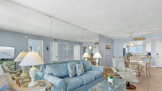A living room with a light blue sofa, wicker chairs, a coffee table, and a dining area with a table and chairs. - Oceania Beach Club 503 (New Smyrna Beach)