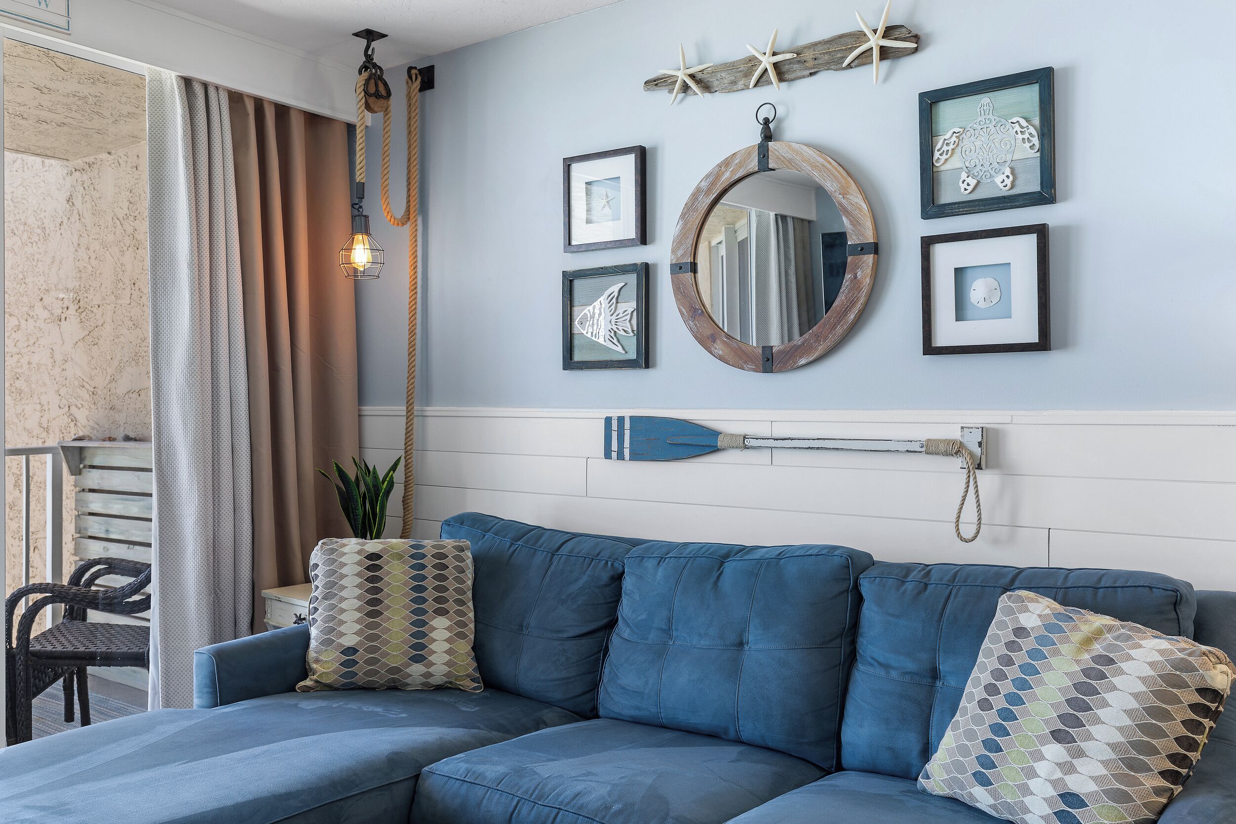 A modern living room with a blue sofa, decorative pillows, a wall-mounted mirror, framed artwork, and a starfish decoration.