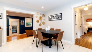 Un coin repas comprenant une table ronde, six chaises et des œuvres d’art décoratives accrochées au mur.