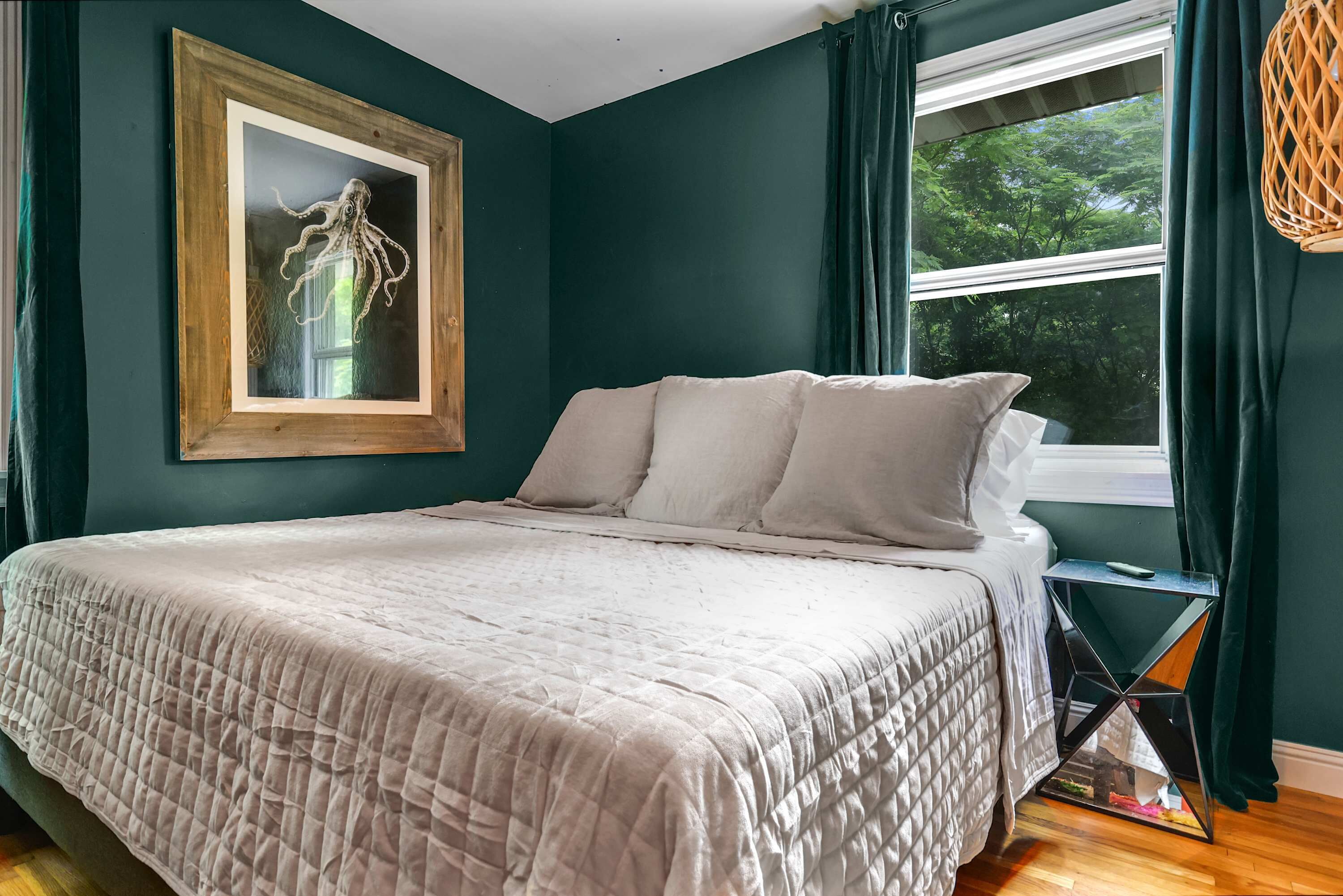 A bedroom with a large bed, a framed artwork on the wall, and a window with curtains.