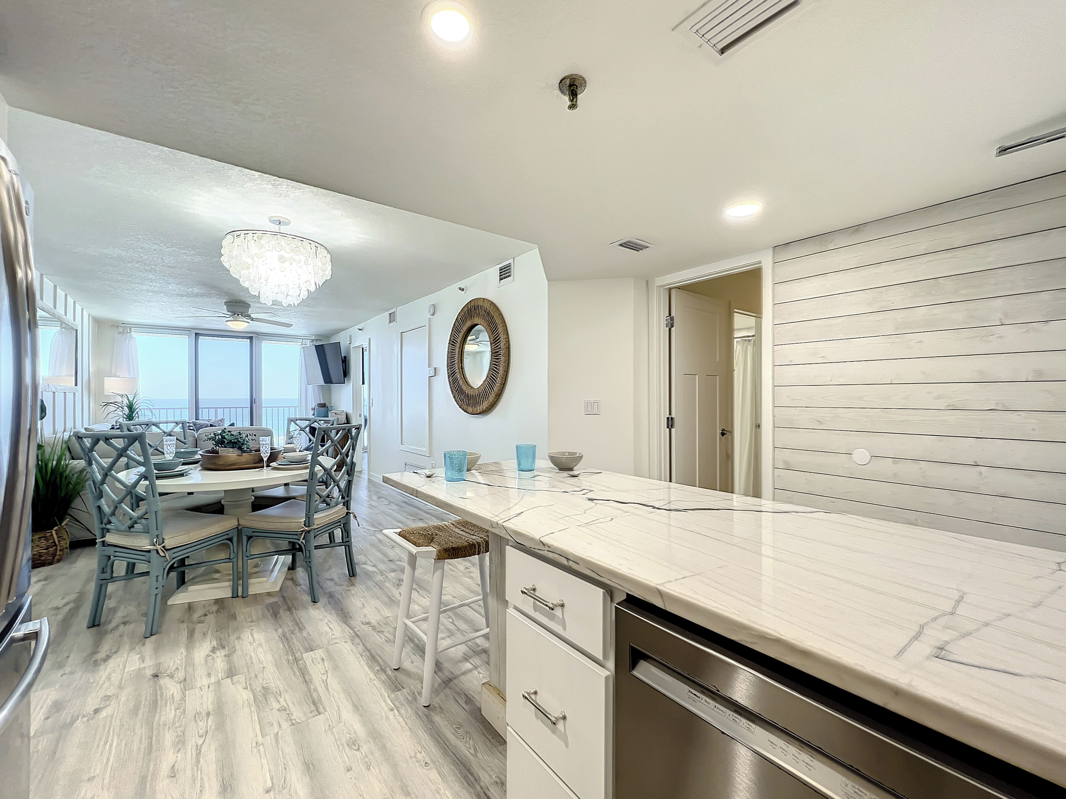 A modern kitchen with a marble countertop, white cabinetry, and a dining area with a chandelier.