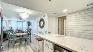Una cocina moderna con encimera de mármol, armarios blancos y un comedor con candelabro.