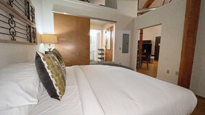 A large bed with white linens and a patterned pillow, a wall with a decorative metal design, and a staircase leading to an upper level. - Writers Round (Nashville)