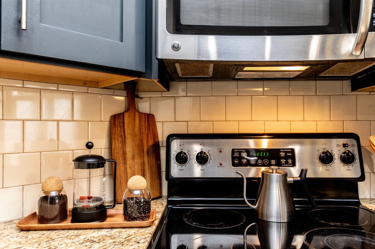 Une cuisine équipée d’une cuisinière en acier inoxydable, d’un four à micro-ondes placé au-dessus, et d’une planche à découper en bois posée sur le plan de travail.
