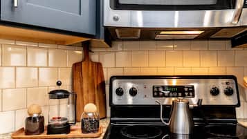 Une cuisine équipée d’une cuisinière en acier inoxydable, d’un four à micro-ondes placé au-dessus, et d’une planche à découper en bois posée sur le plan de travail.