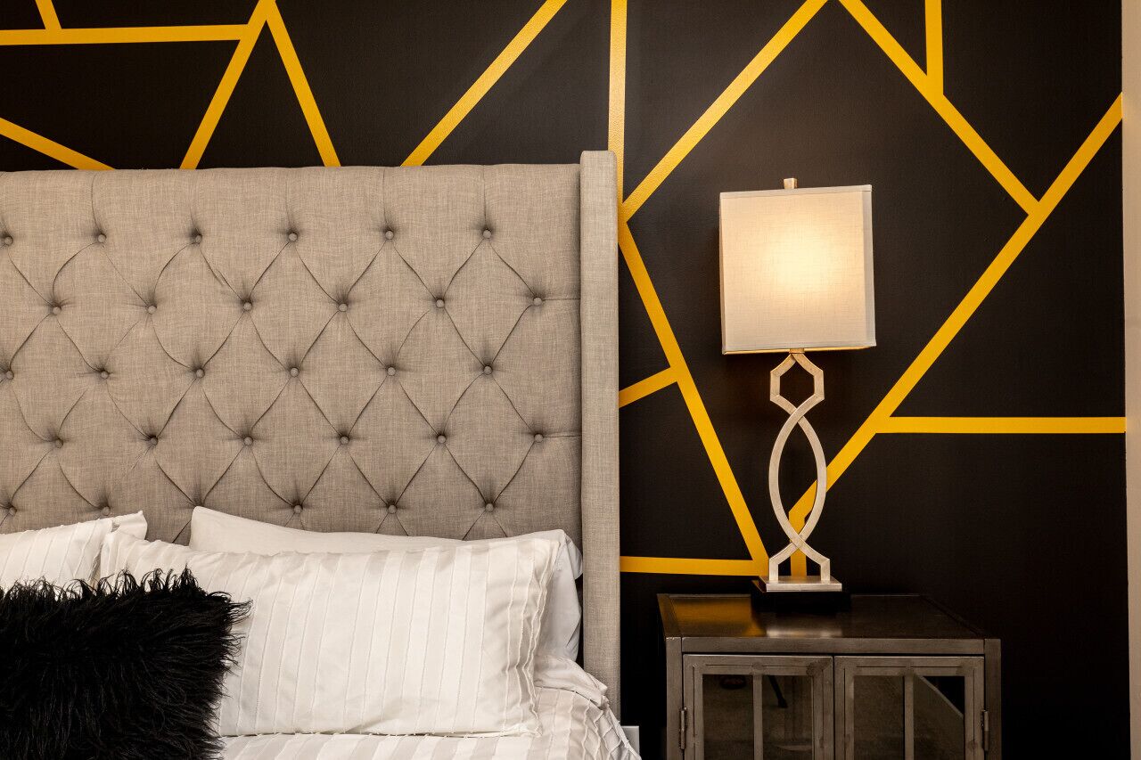 Une chambre à coucher avec une tête de lit capitonnée, une lampe de chevet et un motif géométrique sur le mur.