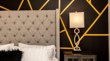 Une chambre à coucher avec une tête de lit capitonnée, une lampe de chevet et un motif géométrique sur le mur.