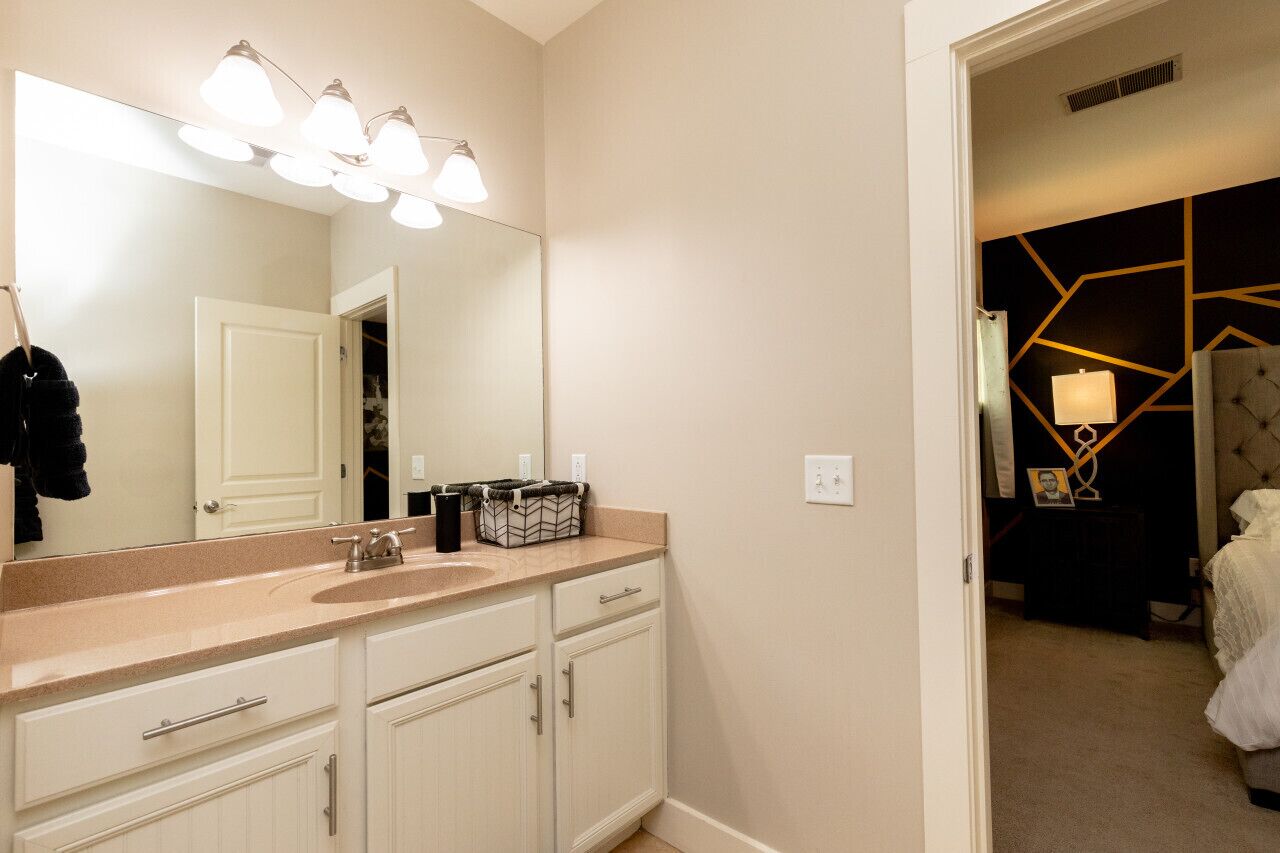 A bathroom with a large mirror, a sink, and a vanity with drawers. There is a door leading to another room.