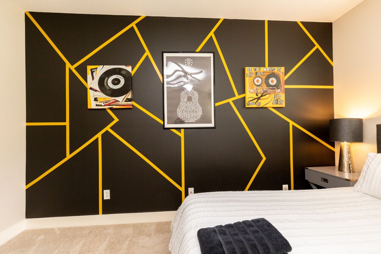 A bedroom with a bed, a nightstand, a lamp, and wall art including a vinyl record and a poster.