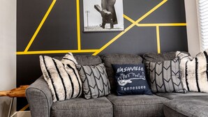 A grey sofa with patterned cushions and a poster on the wall. - Cashville Near Music Row Private Balcony (Nashville)