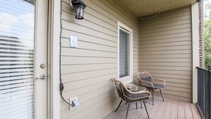 A covered porch with two wicker chairs, a wall-mounted lantern, and string lights. - Cashville Near Music Row Private Balcony (Nashville)