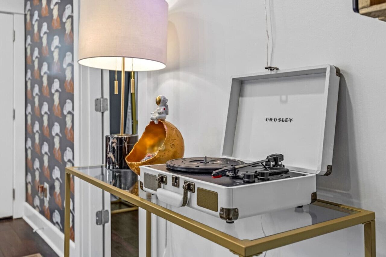 A turntable on a glass table with a gold frame, a lamp, and a wall with a penguin pattern.