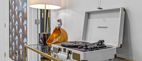 A turntable on a glass table with a gold frame, a lamp, and a wall with a penguin pattern.