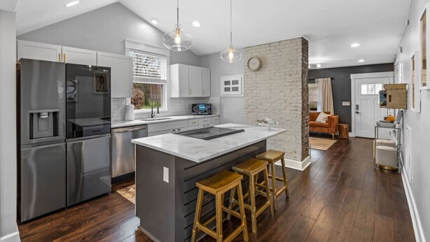 A modern kitchen with a central island, stainless steel appliances, and a brick accent wall. - Space Cowboy - Firepit, Huge Yard, Close2downtown (Nashville)