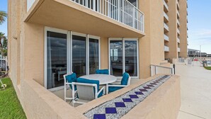 A balcony with a white table and blue chairs, a tiled walkway, and a building with multiple balconies. - Oceania Beach Club 101 (New Smyrna Beach)
